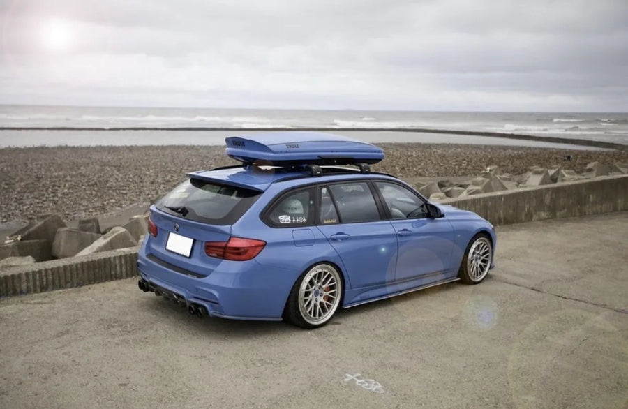 A blue BMW F31 3 Series Touring with a roof box by the sea